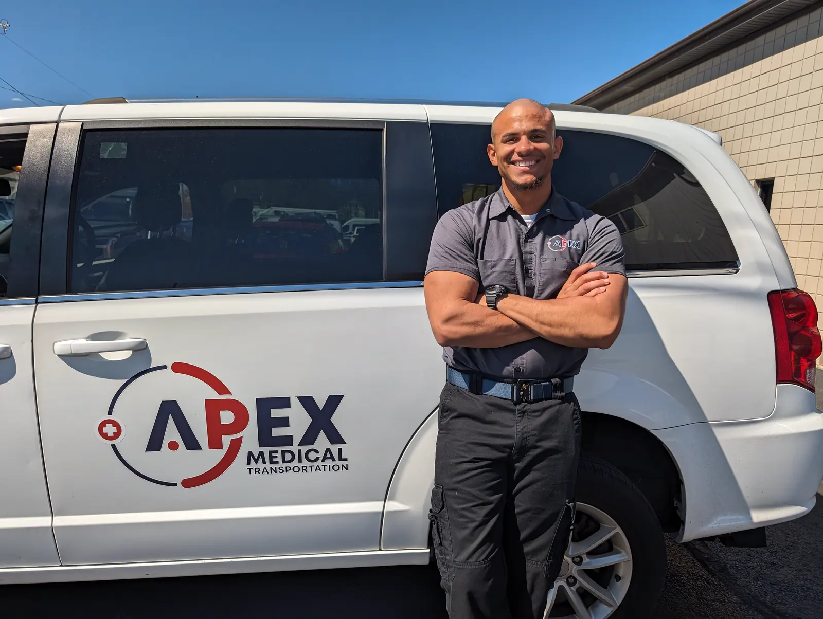 An Apex driver stands with arms crossed in front of an Apex minivan