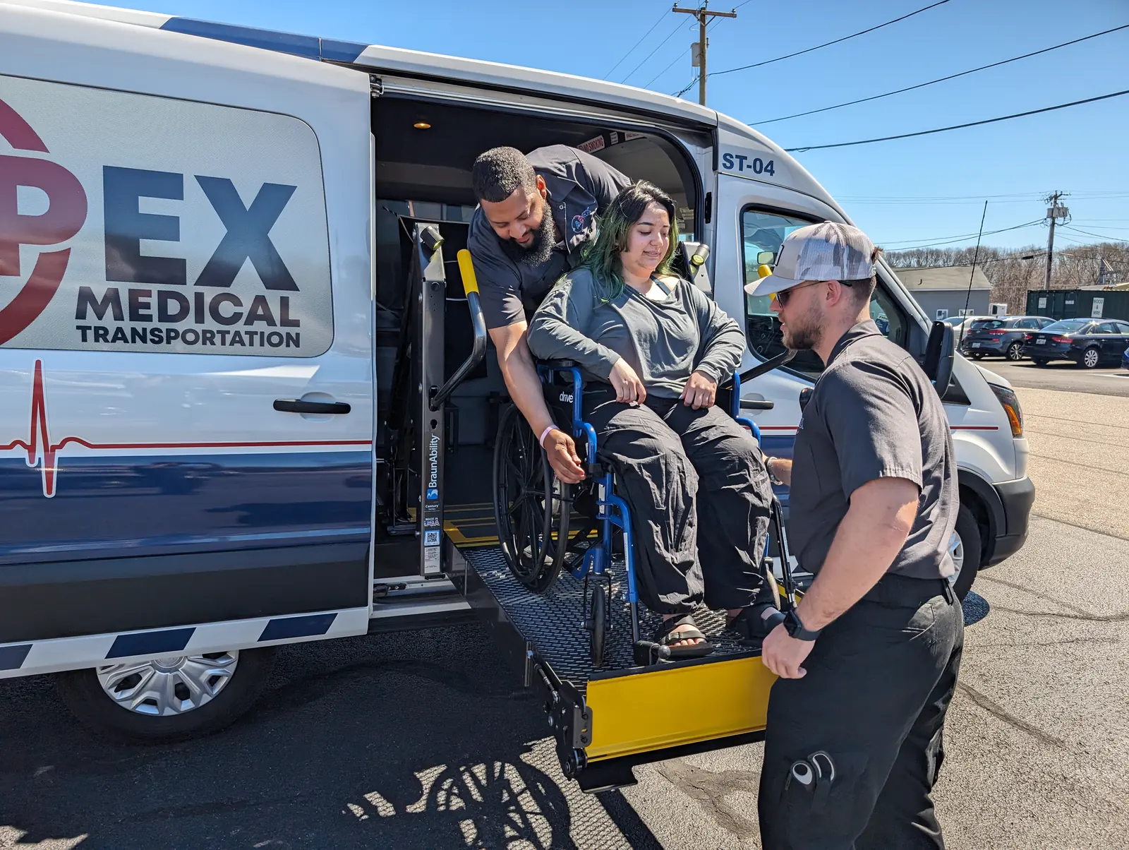 An Apex crew member guides a rider in a wheelchair onto the lift of an Apex wheelchair van
