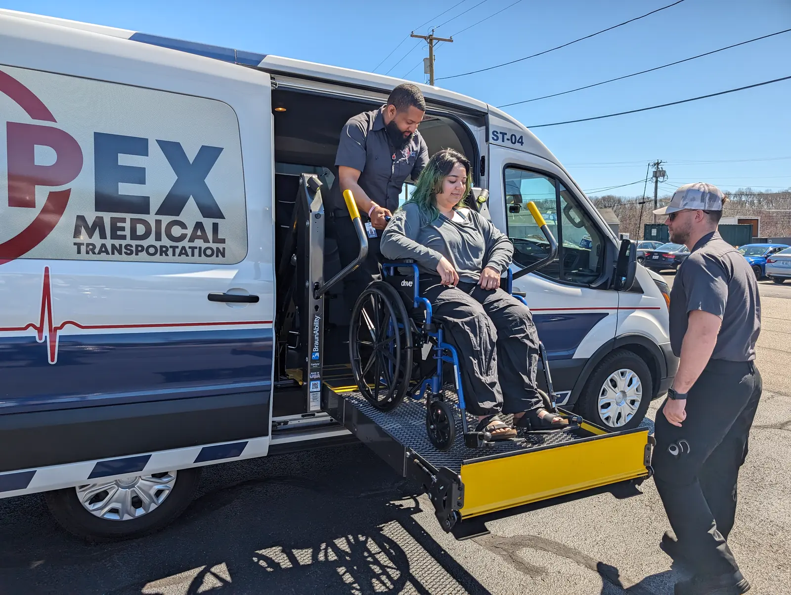 Two Apex crew members bring a rider in a wheelchair down on the lift of an Apex van