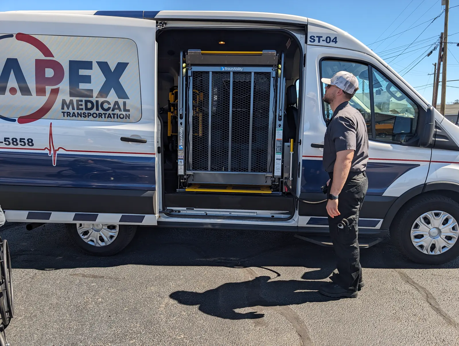 An Apex crew member stands beside an Apex wheelchair van with its side lift open