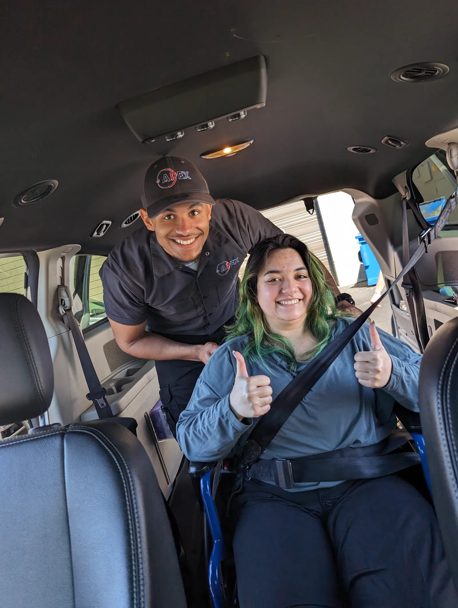 A rider gives a thumbs up from her wheelchair, secured inside an Apex van